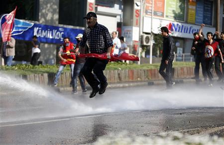 A May Day protester jumps away from a water cannon during clashes between riot police and protesters trying to break through barricades to reach the city's main square in central Istanbul