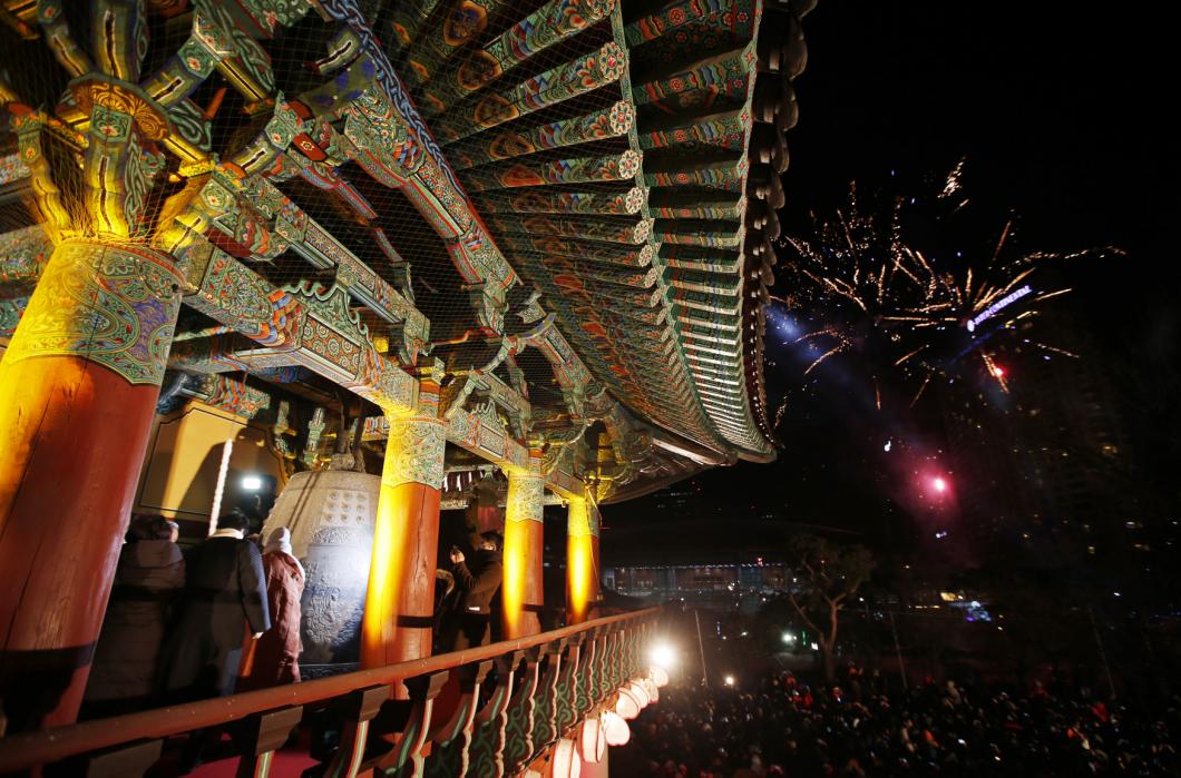 Buddhist monks and believers hit a traditional bell as fireworks go off during a ceremony to celebrate the new year at Bongeun Buddhist temple in Seoul