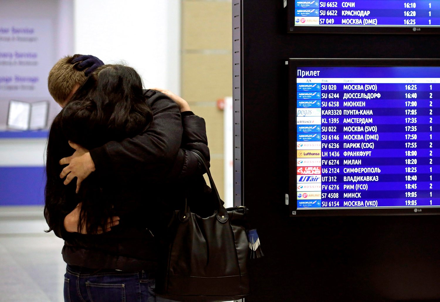 A couple embraces next to a flight information board at Pulkovo airport in St. Petersburg